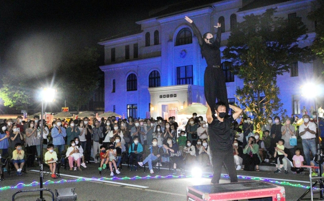 「豊岡演劇祭２０２２」の最終日。路上パフォーマンスを観覧する市民ら＝２５日夜、豊岡市役所前