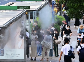 バス停の屋根から霧状の水が出るミスト装置に手をかざし、一瞬の涼を求める人の姿も＝１２日午後、神戸市中央区加納町５