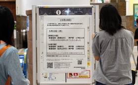 台風１４号の影響で繰り上げられた最終電車の案内板を前に、足を止める利用客たち＝１９日午後２時１６分、ＪＲ神戸駅