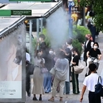 バス停の屋根から霧状の水が出るミスト装置に手をかざし、一瞬の涼を求める人の姿も＝１２日午後、神戸市中央区加納町５