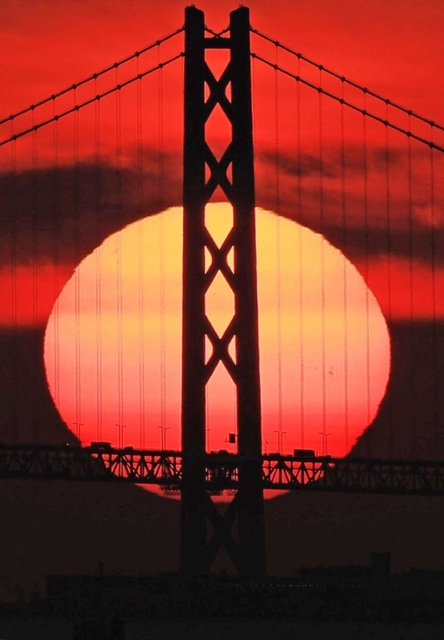 明石海峡大橋の向こうに落ちる夕日。主塔のシルエットがくっきりと浮かび上がった＝２日夕、神戸市中央区の神戸空港から