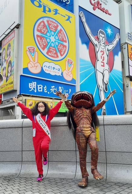 江崎グリコの電光看板前でポーズをとる福崎町ふるさと大使のアルミカン赤阪侑子さん（左）と河童のガジロウ＝大阪市内