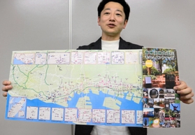 ２１年ぶりに紙製で発行された「震災モニュメントマップ」を掲げる藤本真一さん＝神戸市役所