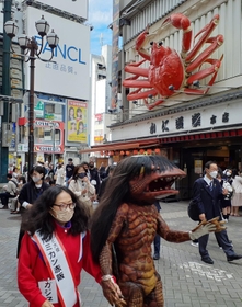 「河童のガジロウ」と手をつないで繁華街を歩くアルミカン赤阪侑子さん＝大阪市内