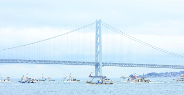 明石海峡大橋を背にパレードする漁船団＝１３日午後２時２４分、兵庫県明石市中崎１から（撮影・鈴木雅之）