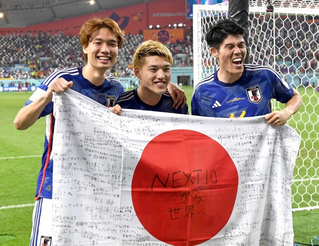 兄の憂さんと運営するサッカースクールの子どもたちが寄せ書きした国旗を手に、笑みを浮かべる堂安（中央）、板倉（左）、冨安＝ドーハ（撮影・金田祐二）
