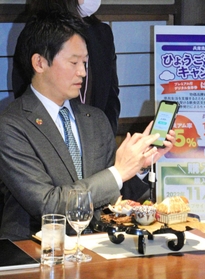 スマートフォンを手に「はばタンＰａｙ（ペイ）」の使い方を説明する斎藤元彦知事＝神戸市東灘区御影塚町１、神戸酒心館