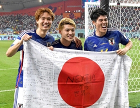 兄の憂さんと運営するサッカースクールの子どもたちが寄せ書きした国旗を手に、笑みを浮かべる堂安（中央）、板倉（左）、冨安＝ドーハ（撮影・金田祐二）