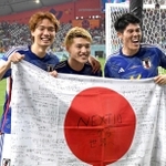 兄の憂さんと運営するサッカースクールの子どもたちが寄せ書きした国旗を手に、笑みを浮かべる堂安（中央）、板倉（左）、冨安＝ドーハ（撮影・金田祐二）