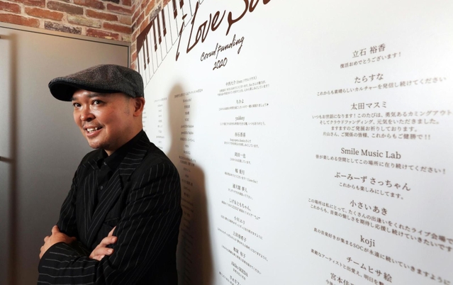 クラウドファンディングで寄せられた応援のメッセージに支えられたという片山行茂代表。ライブハウス「ソープ・オペラ・クラシックス梅田」の入り口に大きく掲示している＝大阪市北区西天満４