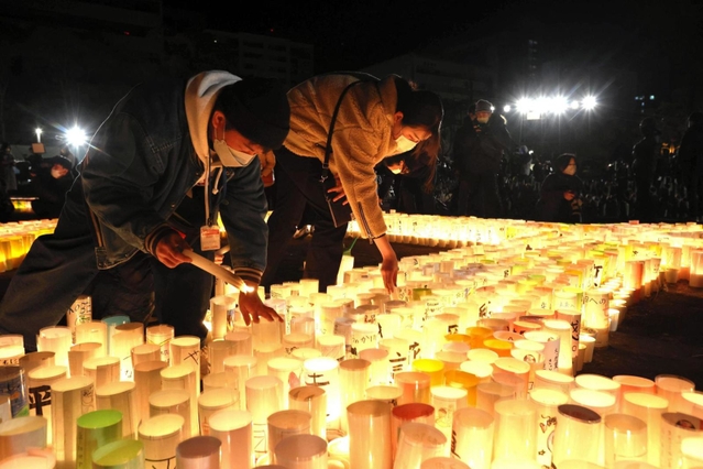 紙灯籠に火をともす人たち＝１７日午前４時４５分、神戸市中央区、東遊園地