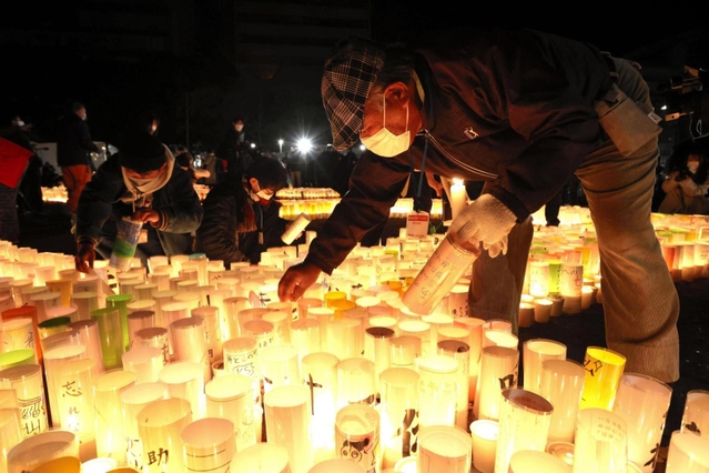 紙灯籠に火をともす人たち＝１７日午前４時４１分、神戸市中央区、東遊園地