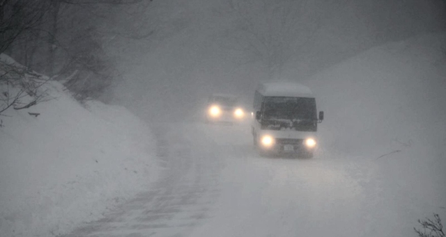 吹雪の中、ライトを付けて徐行する車＝２４日午後、香美町村岡区和池