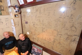 アクリル板で覆った壁を見上げる木下大輔さん（左）と一夫さん。震災の傷もサインも、はっきりと確認できる＝神戸市須磨区大田町２