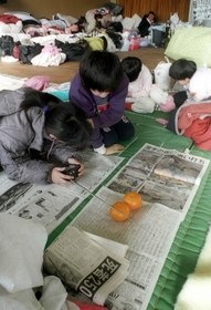 ラジオを手に避難所に届けられた新聞をくいいるように読む被災者＝１９９５年１月１９日、神戸市中央区野崎通、市立上筒井小学校