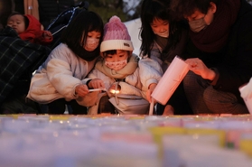 紙灯籠に火をともす子どもら＝１６日午後、神戸市中央区加納町６、東遊園地