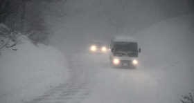 吹雪の中、ライトを付けて徐行する車＝２４日午後、香美町村岡区和池
