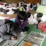 ラジオを手に避難所に届けられた新聞をくいいるように読む被災者＝１９９５年１月１９日、神戸市中央区野崎通、市立上筒井小学校