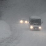吹雪の中、ライトを付けて徐行する車＝２４日午後、香美町村岡区和池