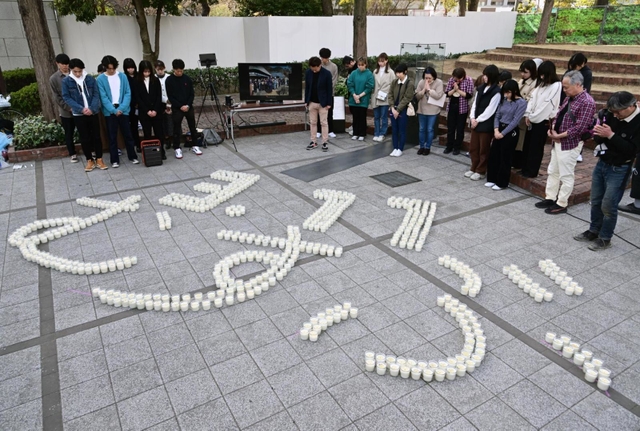 「３・１１　むすぶ」の文字にかたどられたろうそくを囲み、黙とうする参列者＝１１日午後２時４６分、神戸市中央区加納町６