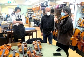 ６台のバイオリンの中から自分にあった１台を探す（右から）ユリヤ・ガブリレンコさんと守山俊吾さん、松永歓社長＝大阪市中央区、国際楽器