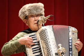 友好の願いを込めてロシア製のミンク帽をかぶり、シベリア抑留体験を弾き語る田中唯介さん＝兵庫県播磨町中央公民館