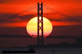 明石海峡大橋の向こうに落ちる夕日。主塔のシルエットがくっきりと浮かび上がる＝２０２２年１０月、神戸市中央区神戸空港から