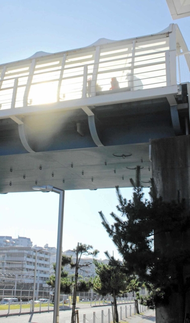 朝日に照らされる歩道橋。慰霊碑に手を合わせる人のシルエットが壁に映る＝明石市大蔵海岸通１