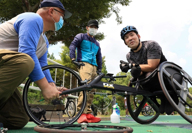 車輪のメンテナンスを担当する朝倉幸雄さん（左）や専属コーチの岩見一平さん（中央）の協力を得て練習する大矢勇気＝６月２５日、神戸市北区、しあわせの村（撮影・吉田敦史）