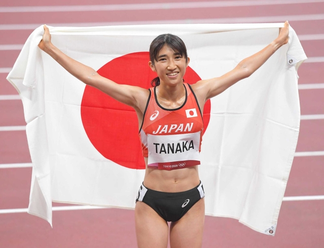 東京五輪の陸上女子１５００メートル決勝で８位入賞し、日の丸を背に笑顔を見せる田中希実＝８月６日、国立競技場
