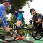 車輪のメンテナンスを担当する朝倉幸雄さん（左）や専属コーチの岩見一平さん（中央）の協力を得て練習する大矢勇気＝６月２５日、神戸市北区、しあわせの村（撮影・吉田敦史）