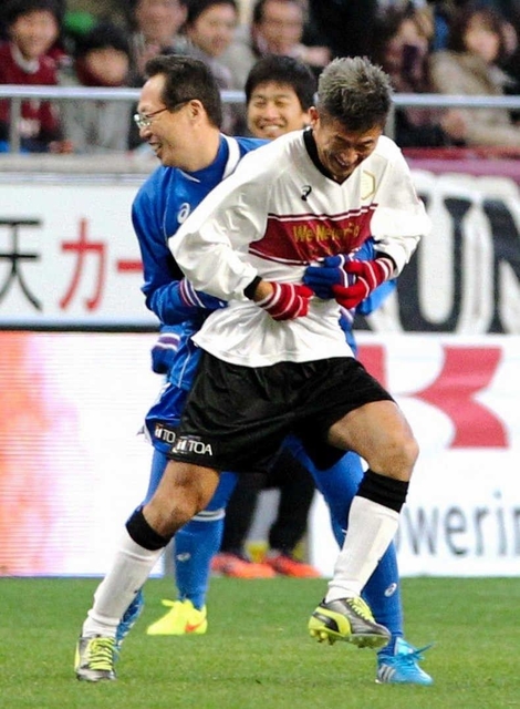 阪神・淡路大震災20年のチャリティーサッカーで、後半、選手として出場した元日本代表監督の岡田武史さんに抱きつかれる横浜ＦＣの三浦知良（右）＝２０１５年１月17日、ノエビアスタジアム神戸