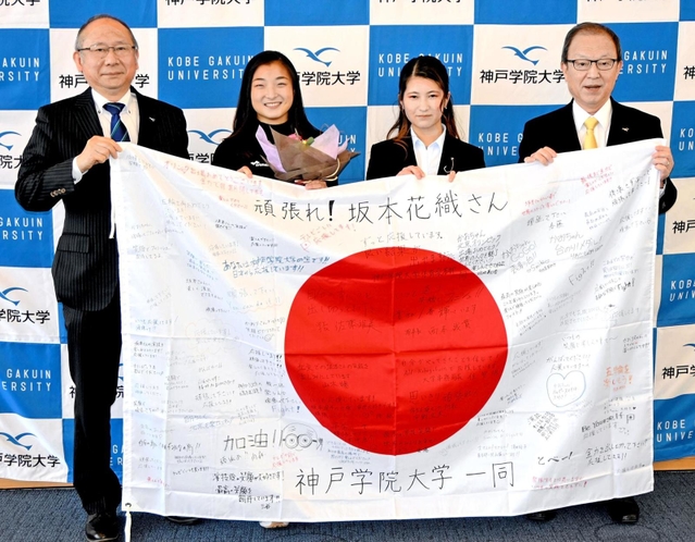 寄せ書きで埋まった国旗を手にする（左から）佐藤雅美学長、坂本花織選手、学生代表中谷綾乃さん、西本誠實理事長＝神戸市中央区港島１、神戸学院大（同大提供）
