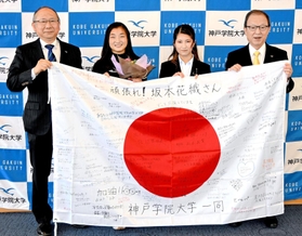 寄せ書きで埋まった国旗を手にする（左から）佐藤雅美学長、坂本花織選手、学生代表中谷綾乃さん、西本誠實理事長＝神戸市中央区港島１、神戸学院大（同大提供）