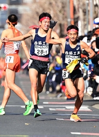男子１区区間賞に輝いた西脇工の長嶋幸宝（左）から２区小田伊織へたすきリレー＝京都市内