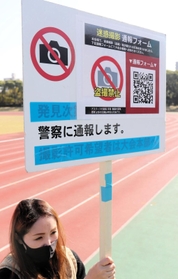 盗撮行為への注意を呼びかける看板を持つ大阪陸上競技協会の担当者＝大阪市東住吉区、ヤンマーフィールド長居