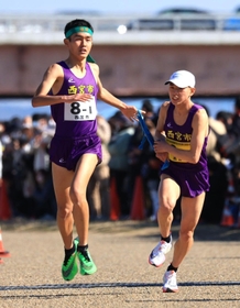 男子１区区間賞に輝いた西宮市の前田和摩（左）からたすきを受ける２区西村稜太＝加古川市の加古川河川敷マラソンコース
