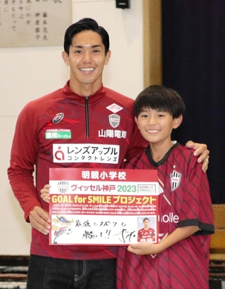 メッセージボードを手に明親小の６年生と記念撮影に納まる神戸のＦＷ武藤嘉紀＝神戸市兵庫区須佐野通４の同校