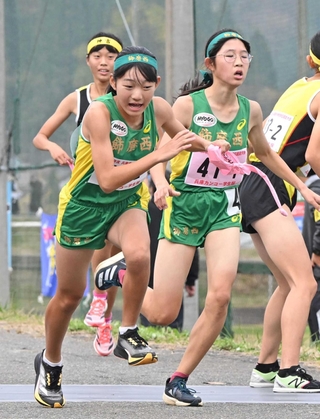 女子・飾磨西の１区堤彩花（右）からたすきを受けて駆け出す２区和田心奈（撮影・大田将之）