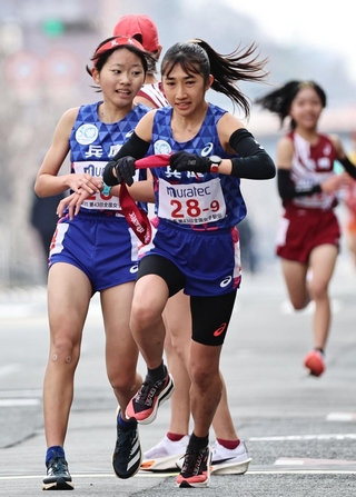 ８区の朝日小都子（左）からアンカーの田中希実にたすきが渡る＝１２日午後、京都市（撮影・長嶺麻子）