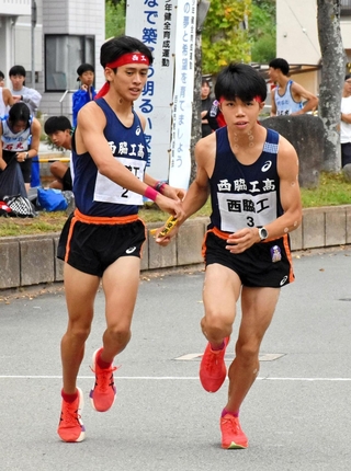 地区予選会で男子・西脇工の中道琉惺（左）からたすきを受け取る新妻昂己＝西脇市総合市民センター