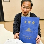 関学大卓球部の百年史を手にする鯛中昌洋さん＝神戸市長田区