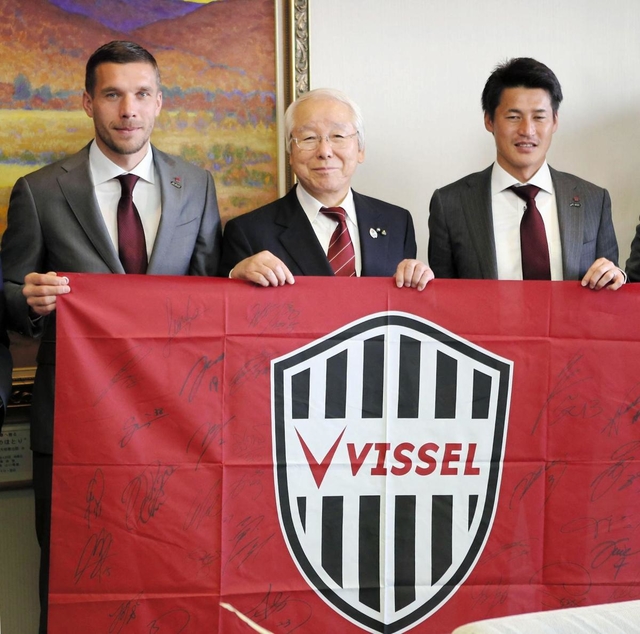 チームのフラッグを持って記念撮影するヴィッセル神戸のポドルスキ主将（左端）と井戸敏三知事（中央）、吉田孝行監督（右端）＝兵庫県庁