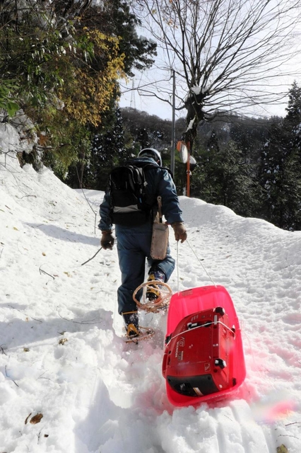 かんじきを履いて雪道を進み、そりに積んだ発電機を運ぶ町職員＝新温泉町高山
