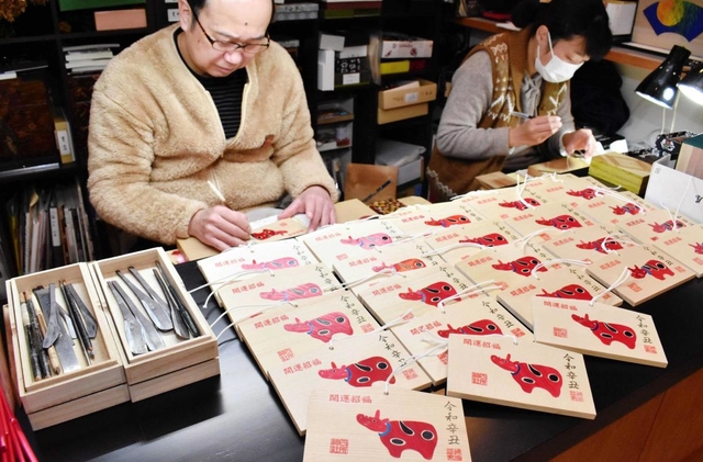 麦わら細工で「赤べこ」をあしらった絵馬を制作する神谷俊彰さん（左）＝かみや民芸店