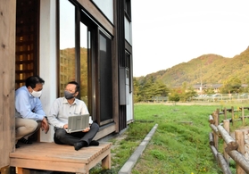 自然に囲まれた「豊岡市エコハウス」で業務に取り組む石光商事の石脇智広社長（左）ら＝豊岡市城崎町今津