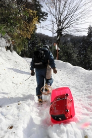 かんじきを履いて雪道を進み、そりに積んだ発電機を運ぶ町職員＝新温泉町高山