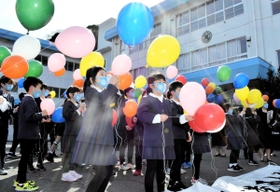 校舎の前で記念の風船を飛ばす子どもたち＝港西小