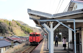 海岸沿いの集落横を走る浜坂発鳥取行きの普通列車＝１４日午前９時ごろ、ＪＲ諸寄駅