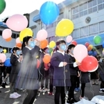 校舎の前で記念の風船を飛ばす子どもたち＝港西小